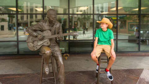 Young boy sitting next to a statue of Chet Atkins in Nashville, TN