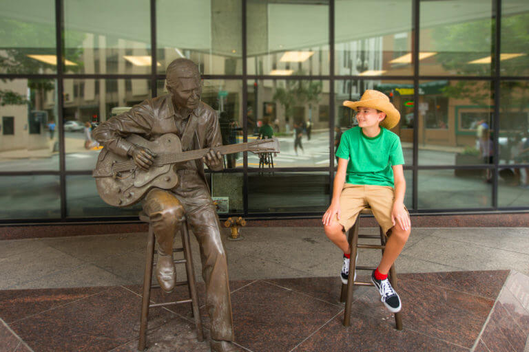 Young boy sitting next to a statue of Chet Atkins in Nashville, TN