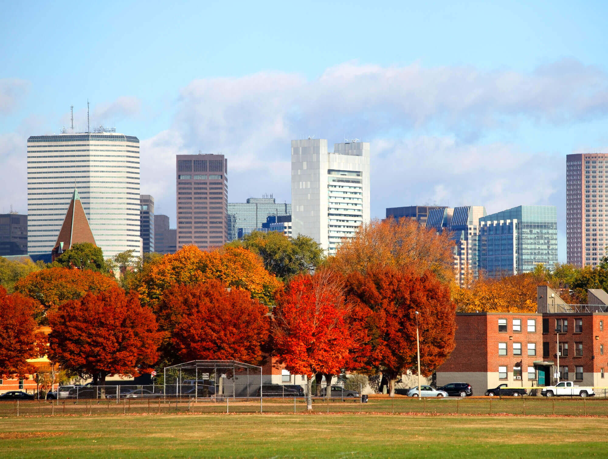 Municipal baseball field surrounded by vivid trees in fall colors with Boston, MA buildings looming