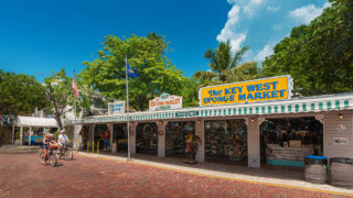 Two people biking along Mallory Square in front of various shops in Key West, FL