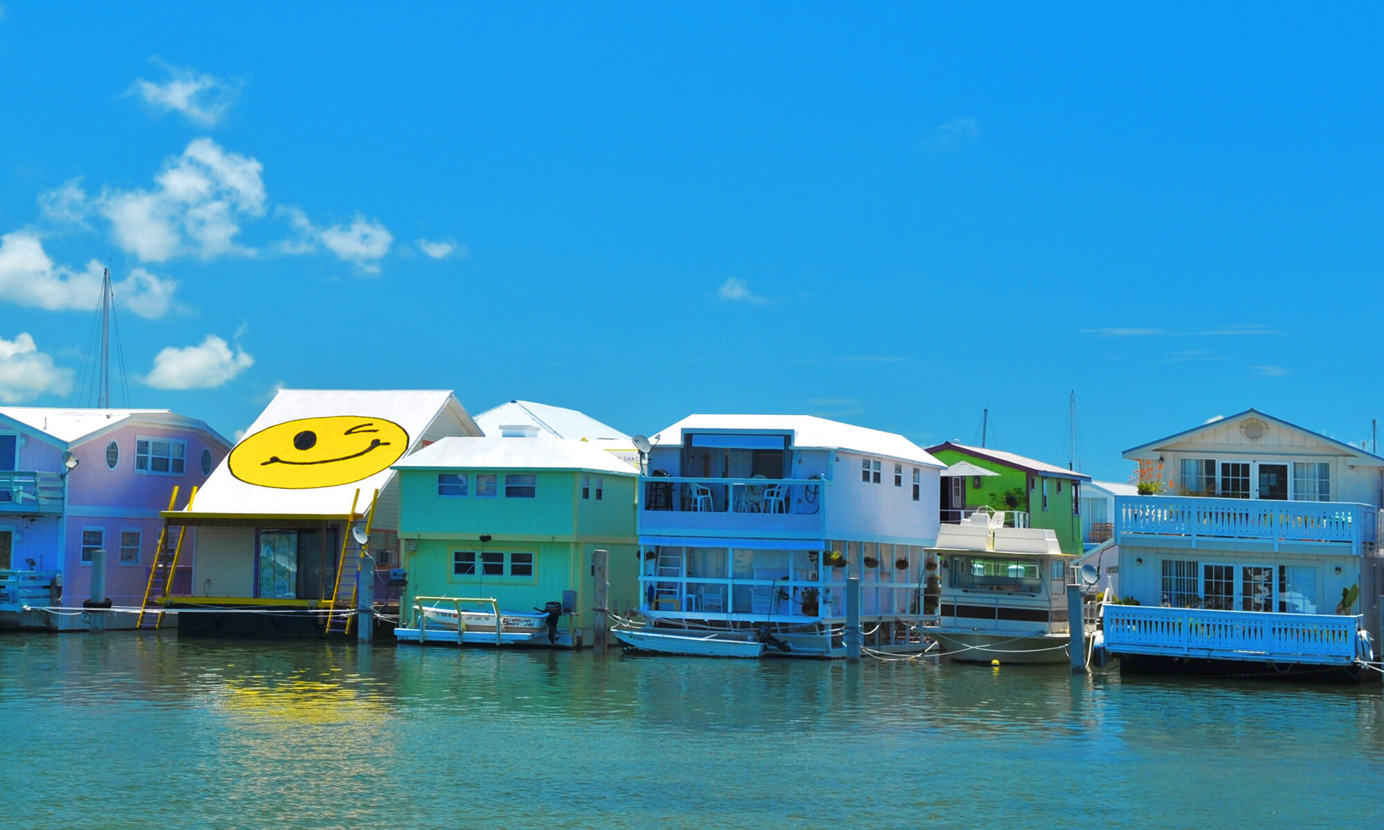 A row of house boats on the water and one of them has a large yellow winking face painted on the roof in Key West, FL