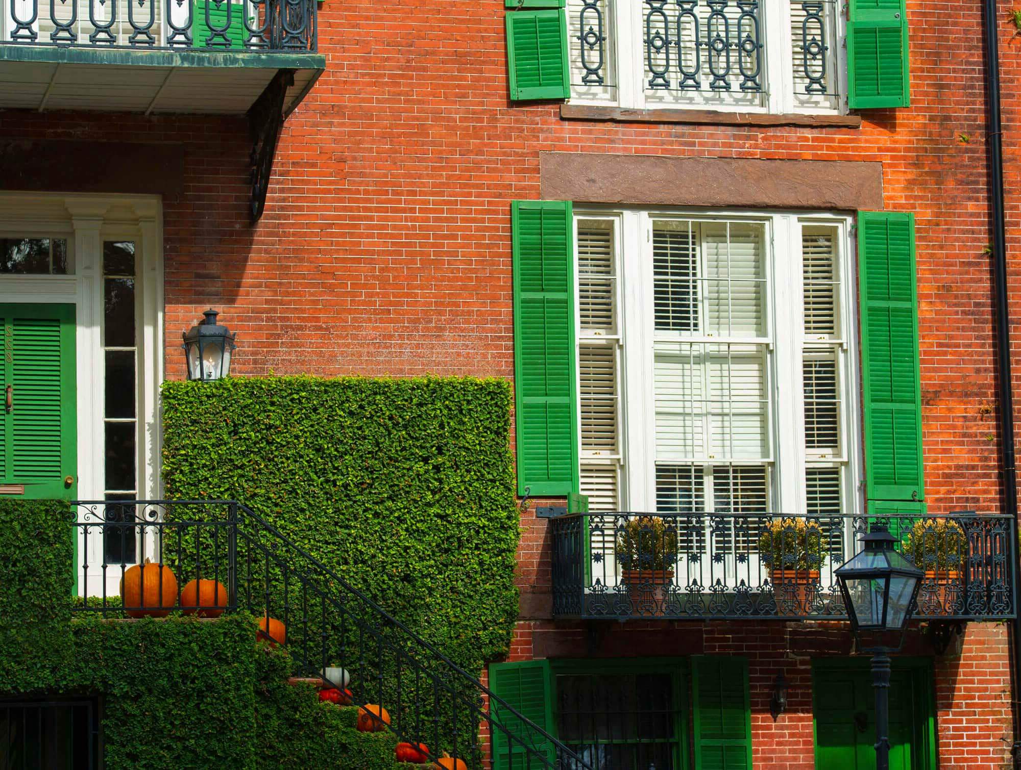 Close-up of a red brick facade with a wrought iron balcony and pumpkins resting on each of the front steps in Savannah, GA