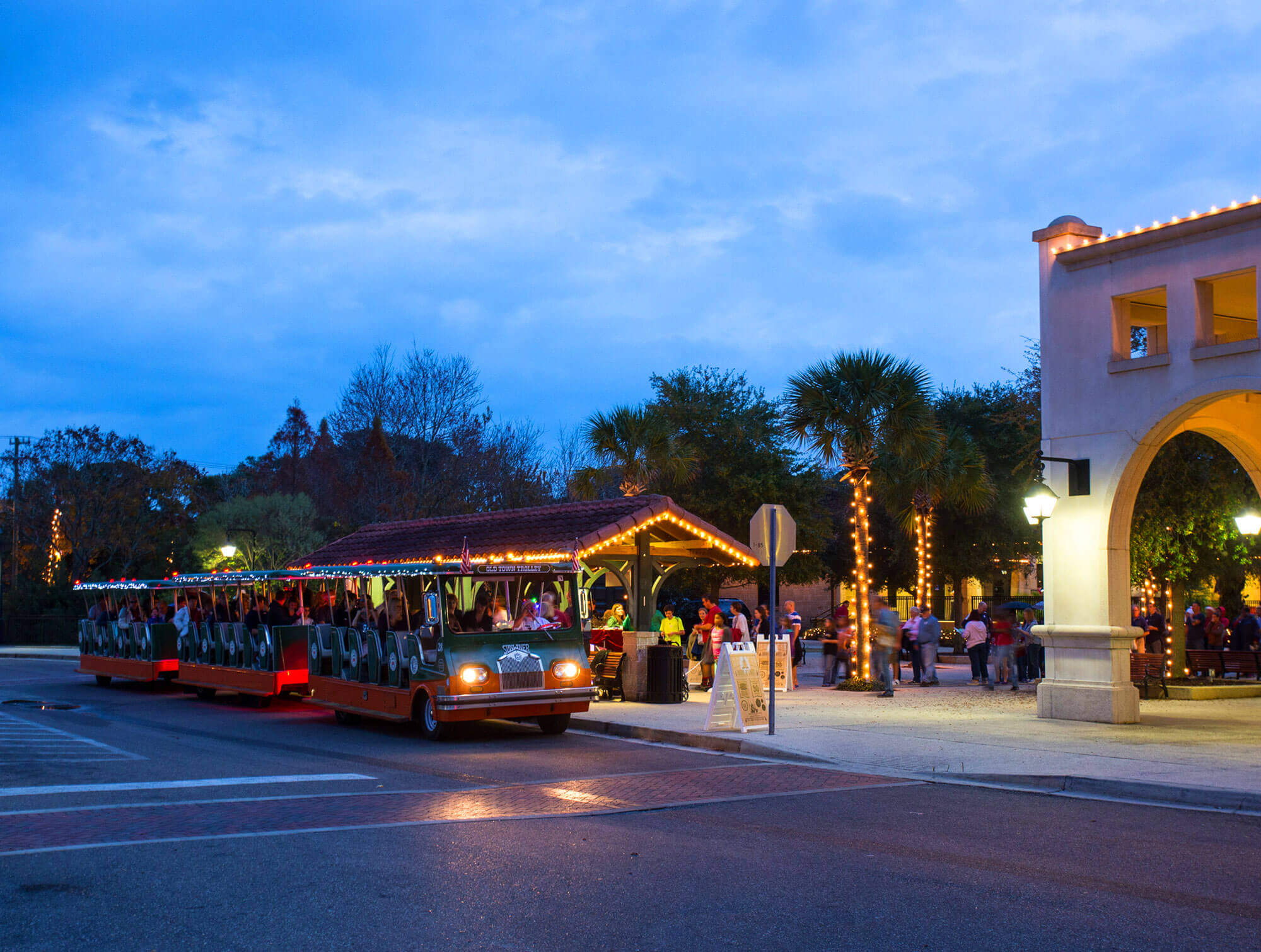 An Old Town Trolley decked out in Christmas lights riding by an outdoor plaza decorated for the holidays in St. Augustine, FL