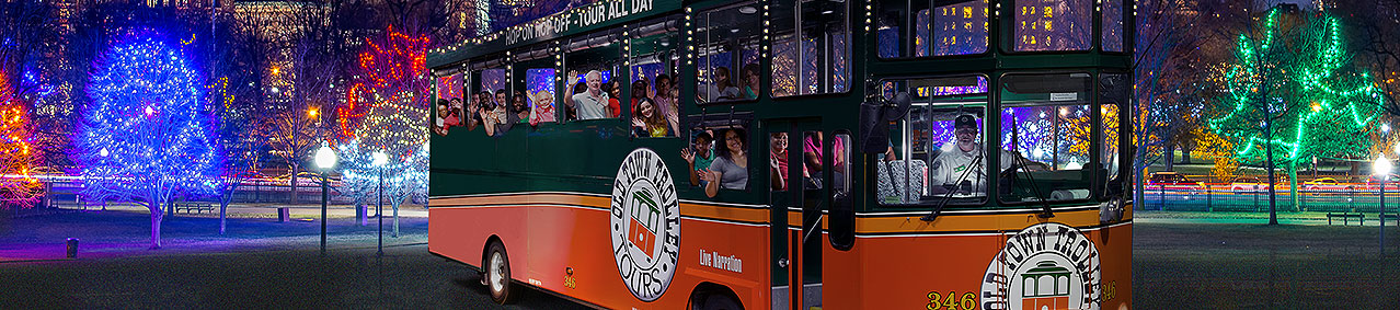night time picture of trolley in front of Boston skyline and holiday lights