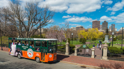 old town trolley in Boston driving past Boston Public Garden and George Washington Statue and city skyline in background