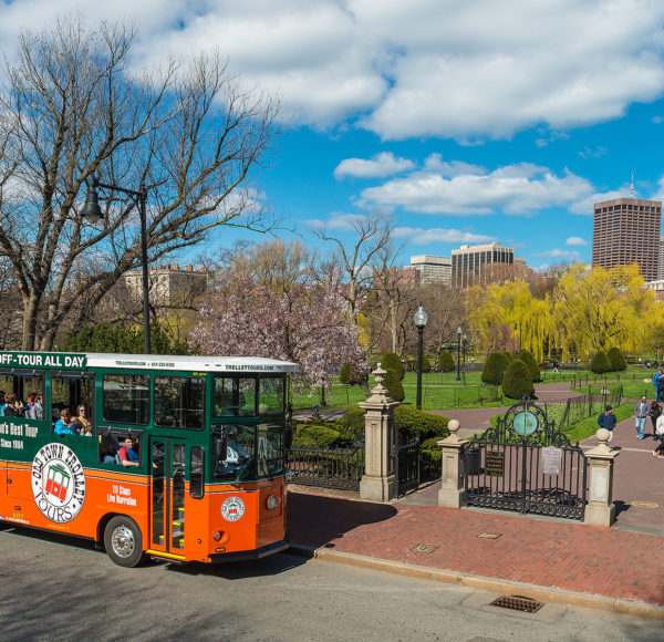 old town trolley in Boston driving past Boston Public Garden and George Washington Statue and city skyline in background