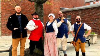 Boston Field Trip Tours - a group of one woman and five men in Boston standing in front of a tree and wearing colonial period clothing