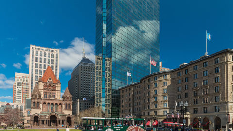 Boston Old Town Trolley driving by Trinity Church and various buildings in the background