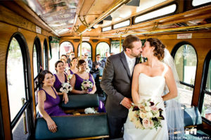 interior of a trolley featuring a bride and groom standing and kissing and the wedding party seated and watching them in the background