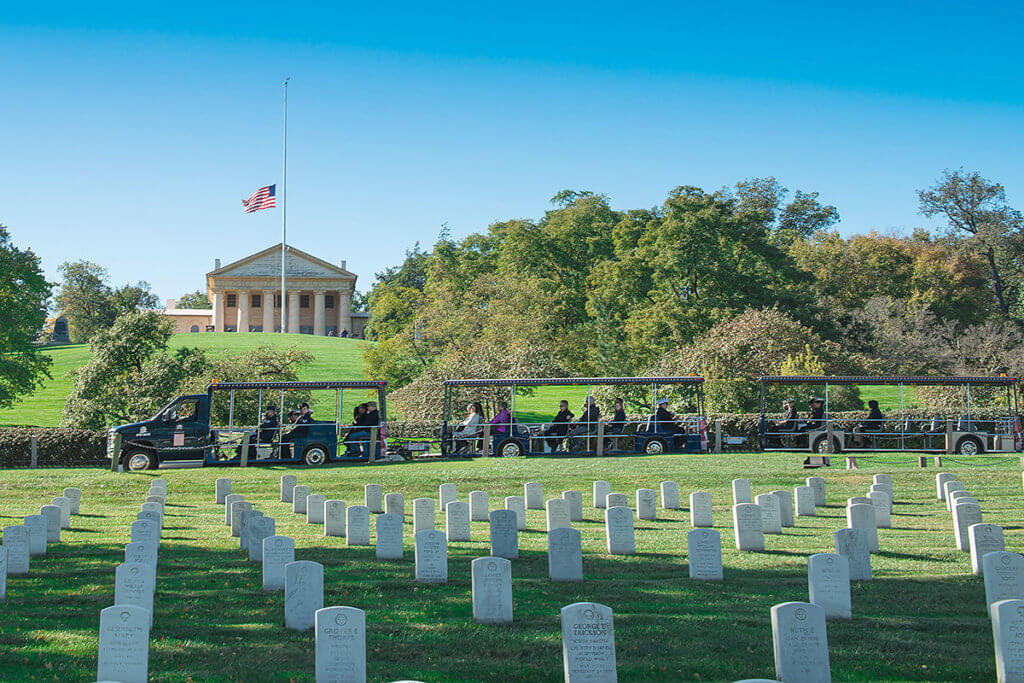 picture of arlington national cemetery vehicle driving past arlington house and tombstones in foreground