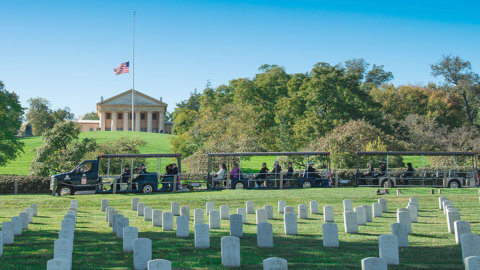 picture of arlington national cemetery vehicle driving past arlington house and tombstones in foreground