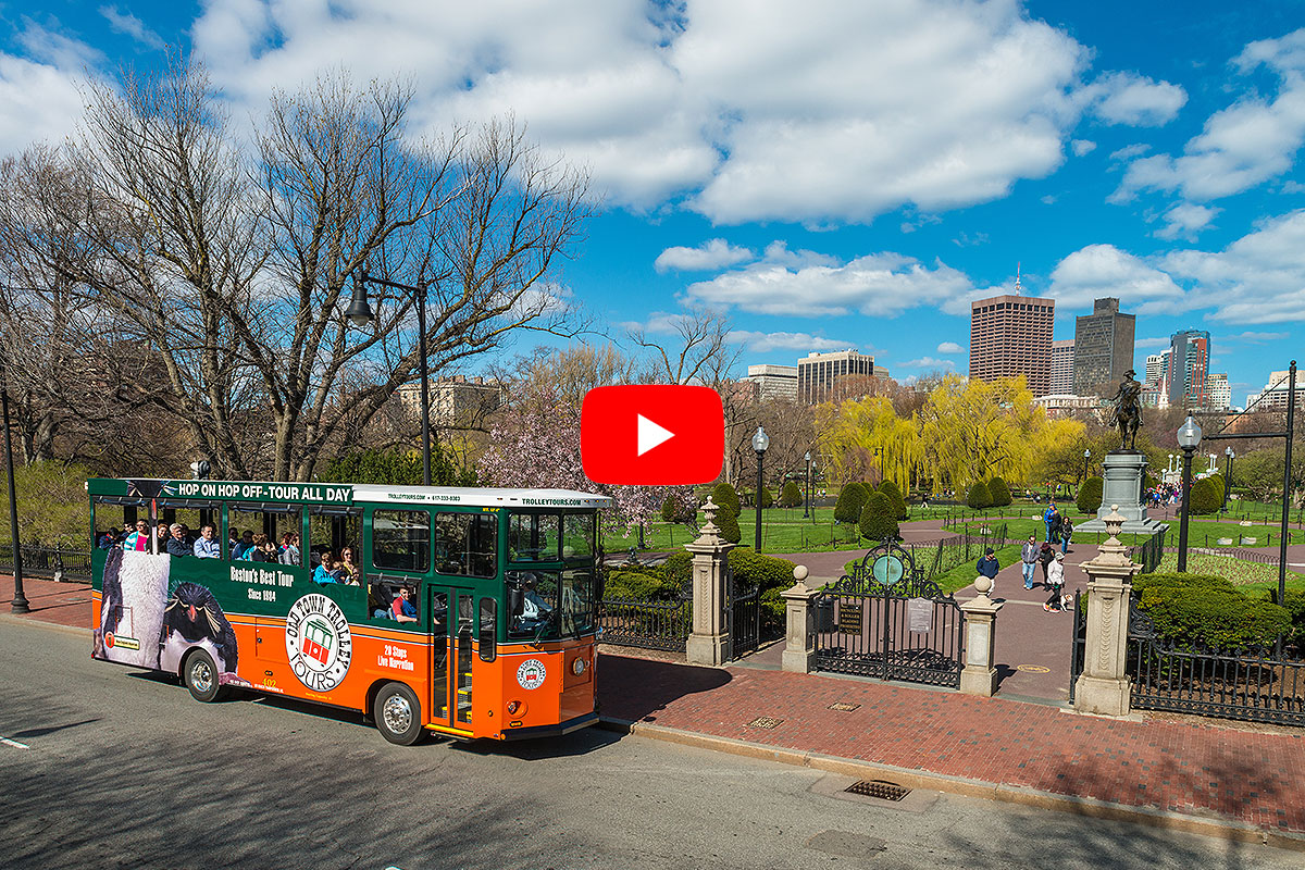 boston old town trolley driving past public garden and city skyline in background