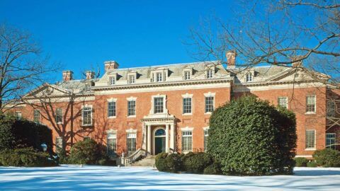view of of front of large historic home made of brick with trees and snow in foreground