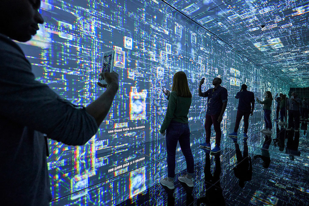 indoor exhibit at international spy museum showing guests holding phones and standing in front of a wall to wall, floor to ceiling digital wall