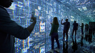 indoor exhibit at international spy museum showing guests holding phones and standing in front of a wall to wall, floor to ceiling digital wall