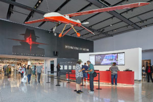 lobby of International Spy Museum in Washington DC showing visitors at concierge desk or coming out of gift shop; on the ceiling is a hanging airplane and on the wall is a picture of a man wearing coat and hat and the words 'Spy Museum Store'