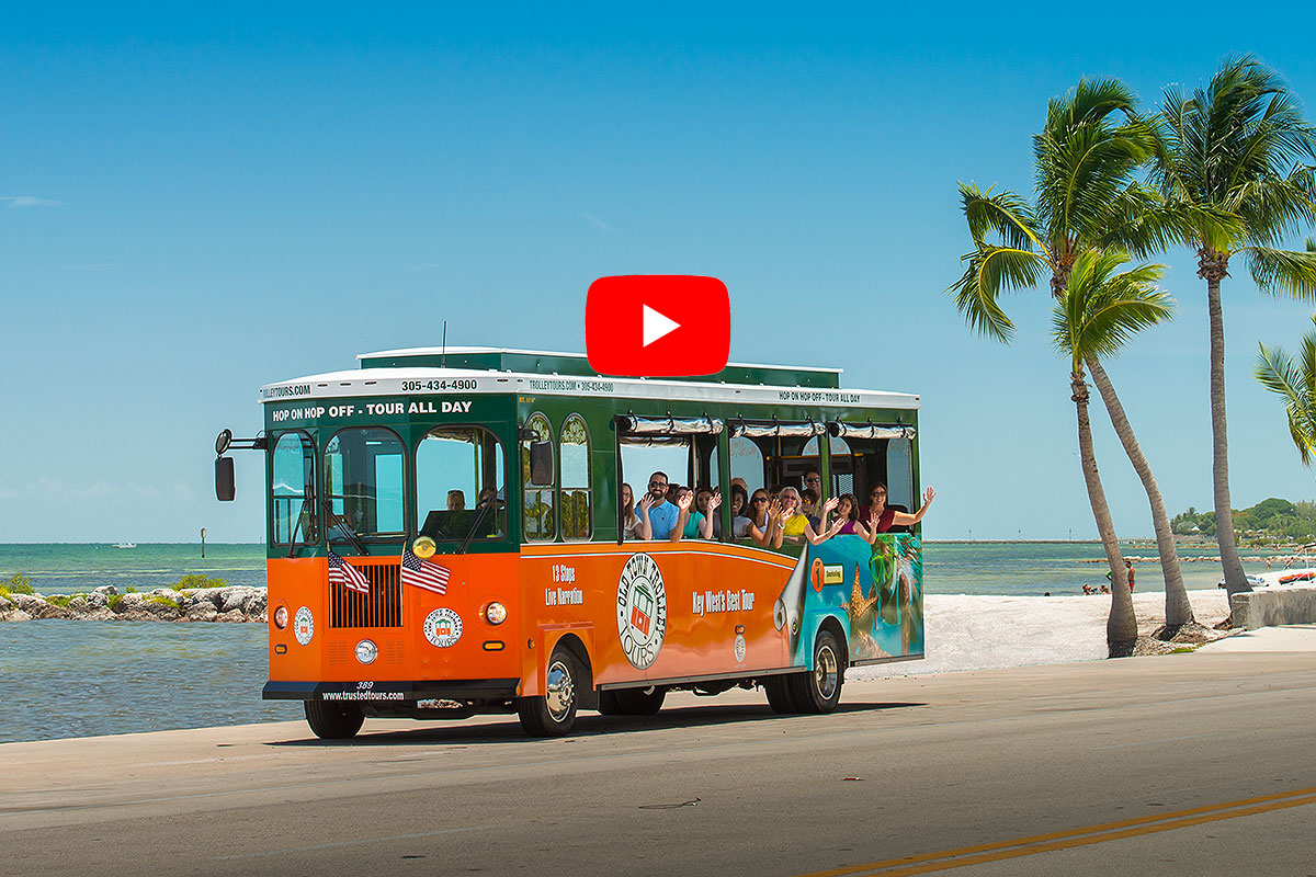 picture of old town trolley in key west driving past ocean and palm trees with a video play button symbol over image