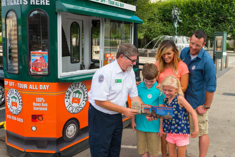 An Old Town trolley ticket agent standing in front of a kiosk with a map in his hand showing a family about to ride the trolley in Nashville, TN