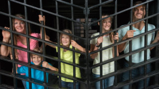 picture showing family of five smiling and standing behind bars inside a cell at the Old Jail Museum