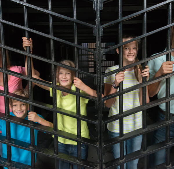 picture showing family of five smiling and standing behind bars inside a cell at the Old Jail Museum