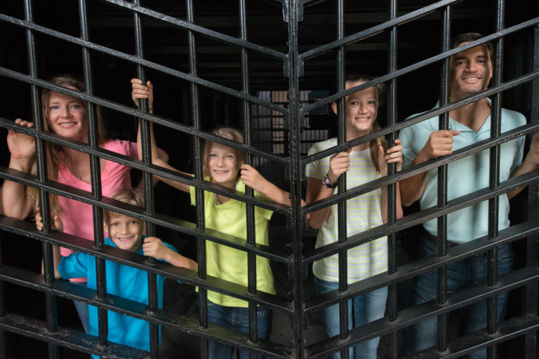 picture showing family of five smiling and standing behind bars inside a cell at the Old Jail Museum