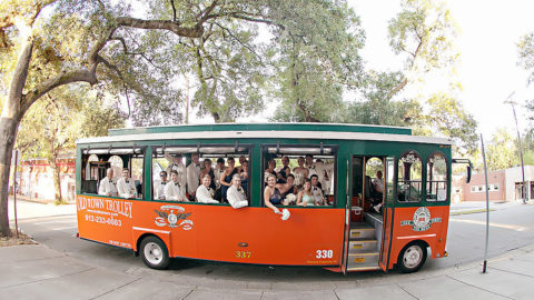 side view of a trolley in Savannah with open windows and wedding party looking on