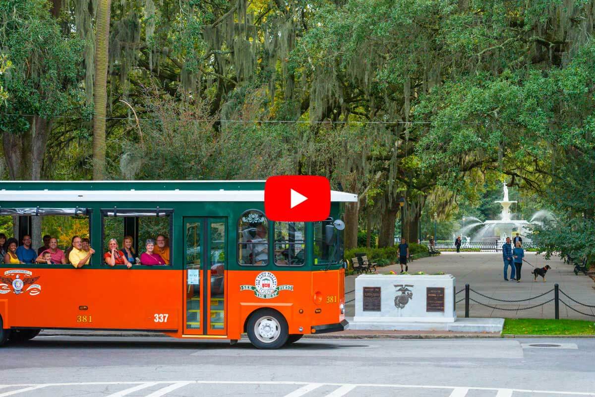 People posing for a picture inside an Old Town Trolley Tour stopped in front of a wooded area of Forsyth Park with Spanish Moss in Savannah, FL