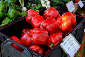 picture of peppers at a farmers market with a sign that reads 'Green Peppers 2/1.00, Red Peppers 1.00 each'