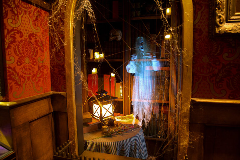 indoor picture of a spooky looking room with a library, table, lantern, spider webs and a ghost