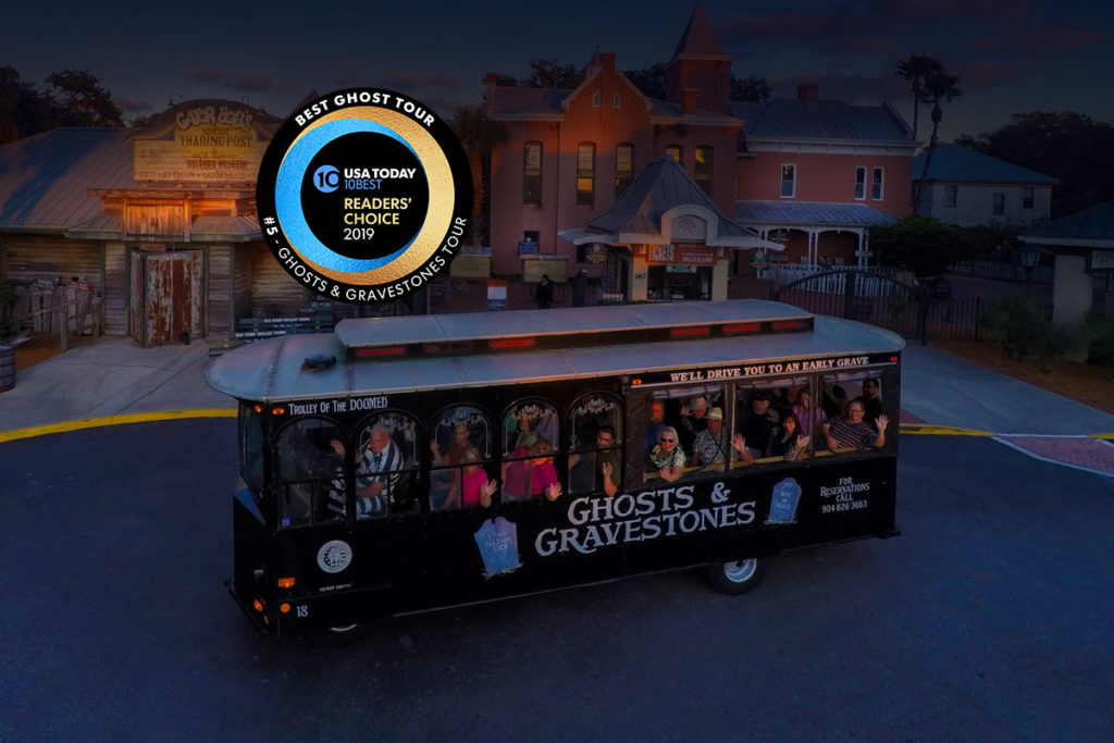 Night time picture of St. Augustine ghost trolley in front of the Old Jail and a Round logo that reads USA Today 10 BEST READERS' CHOICE 2019' and around logo, the words 'BEST GHOST TOUR, #5 - GHOSTS & GRAVESTONES TOUR'