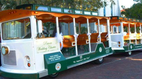 A modified wedding Old Town Trolley painted in white and green parked outside a church in St. Augustine, FL