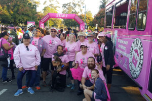group of walkers wearing matching pink shirts standing in front of start line and next a a pink trolley