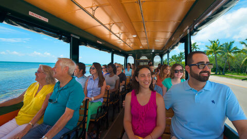 Smiling patrons in bright colored clothes riding next to the beach in Key West during an Old Town Trolley Tour