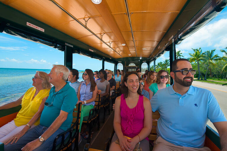 Smiling patrons in bright colored clothes riding next to the beach in Key West during an Old Town Trolley Tour