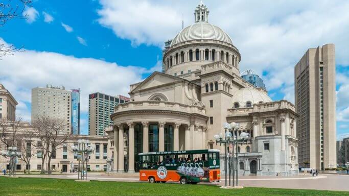 Outside the Christian Science Plaza in Boston where can be seen an Old Town Trolley in front of the Mother Churchmobile