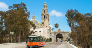 san diego trolley driving past Balboa Park tower behind trolley surrounded by tall trees on both sides