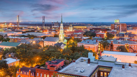 Savannah, Georgia skyline at dusk featuring rooftops in the foreground and Talmadge Bridge in the background