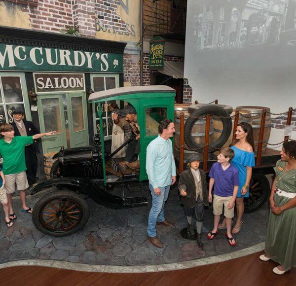 Several patrons of the American Prohibition Museum in Savannah surrounded by wax figures depicting people from that era including an old pickup truck hauling barrels of beer