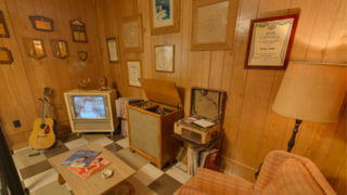 museum display at Patsy Cline Museum showing vintage living area with wood paneling, TV, guitar, lamp, and framed artwork on wall