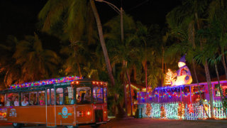 picture of key west old town trolley at night driving past a house decorated with holiday lights