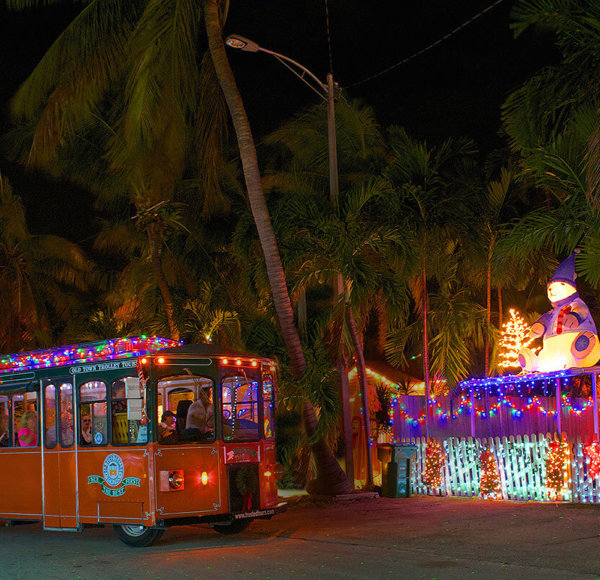 picture of key west old town trolley at night driving past a house decorated with holiday lights