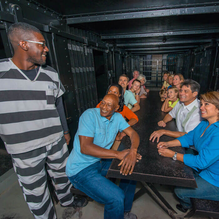 Group of guests sitting on a picnic-style table inside cell at the Old Jail Museum in St. Augustine, FL and listening to tour guide standing