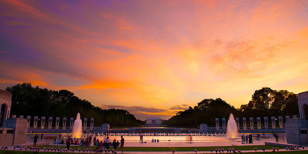 sunset picture of WWII memorial in Washington DC made up of columns and fountains and the Lincoln Memorial far off in the background