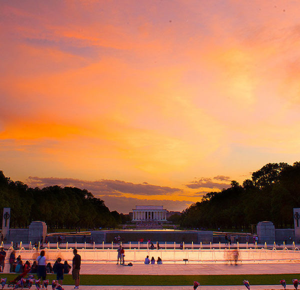 Sunset picture of WWII memorial in Washington DC made up of columns and fountains and the Lincoln Memorial far off in the background