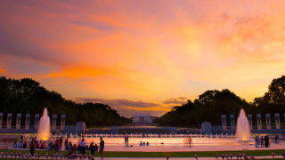 Sunset picture of WWII memorial in Washington DC made up of columns and fountains and the Lincoln Memorial far off in the background