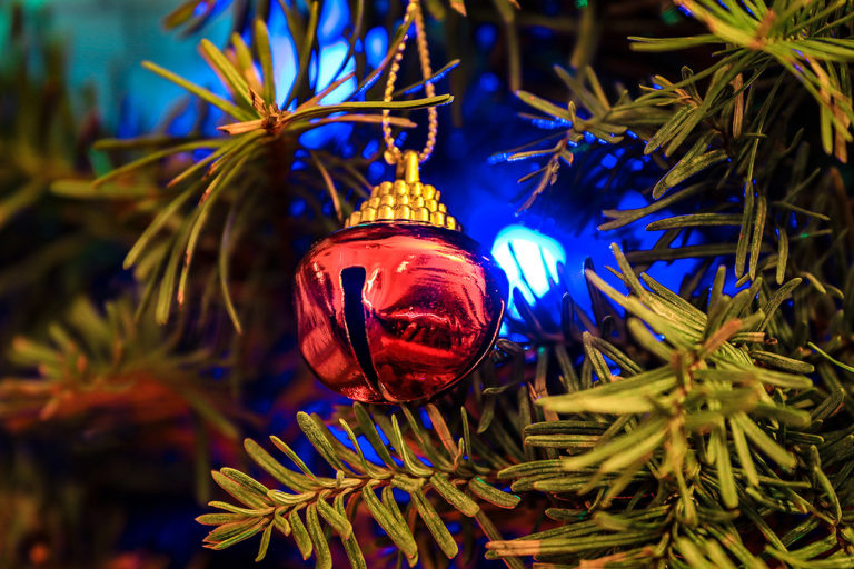 close up picture of a Christmas tree with holiday lights and a bell ornament