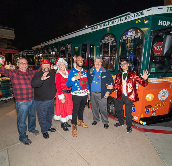San Diego holiday tour guests standing with host in front of trolley