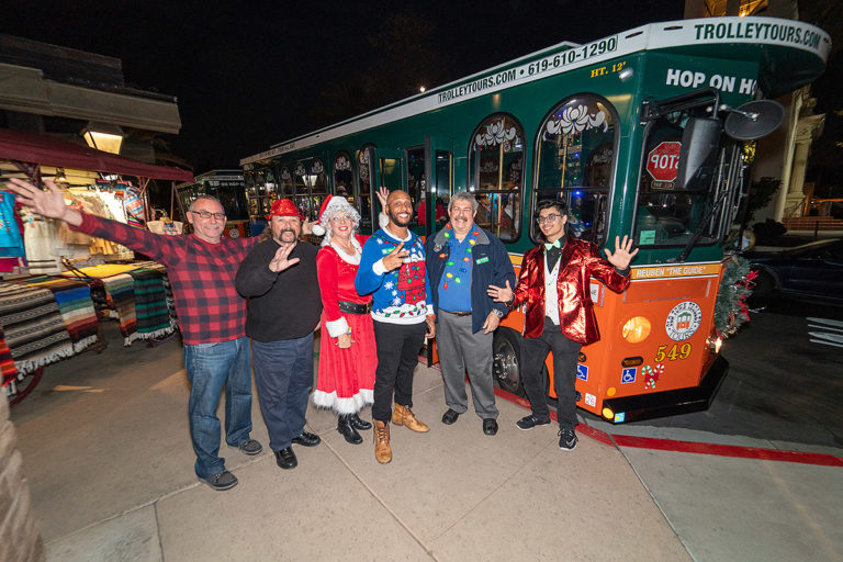 San Diego holiday tour guests standing with host in front of trolley
