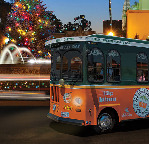 San Diego trolley holiday tour driving at night past Balboa Park with a fountain, historical building and Christmas tree behind it