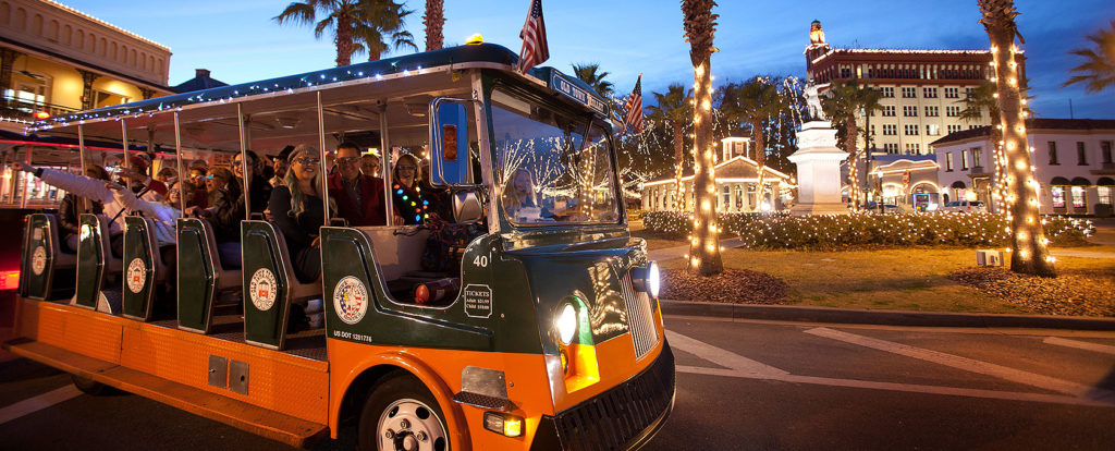st. augustine holiday trolley driving at night past various buildings lit up with holiday lights